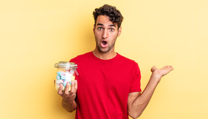 hispanic handsome man looking surprised and shocked, with jaw dropped holding an object. candies concept