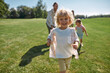 © Svitlana - Joyful little boy smiling while playing catch together with his parents and sister in green park on a summer day. Happy family enjoying leisure activity