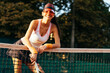 © Westend61 - Happy female tennis player leaning on net at sports court