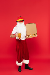 Wall Mural - Father christmas in sunglasses holding mug of beer and pizza on red background