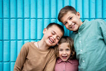 Happy Girl And Boys Standing Together In Front Of Blue Wall