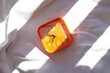 Orange alarm clock in a ray of sun on a white blanket with contrasting shadows