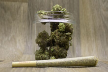 Purple Marijuana Buds In A Glass Jar On A Dark Grey Wooden Background.