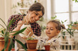 © Tatyana - Mixed race family young happy woman and her daughter is planting and watering houseplants at home.Home gardening.Family leisure, hobby concept.Biophilia design and urban jungle concept.