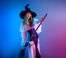 a girl in a witch costume for Halloween with a broom and a pumpkin in neon light