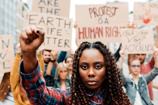 portrait of an african american woman with clenched fist in a global climate strike - group of young
