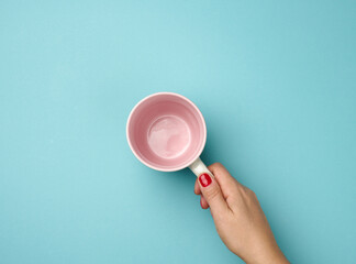 Wall Mural - female hand holds a ceramic mug on a blue background, break time and drink coffee