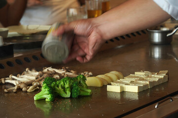 Poster - Chef seasoning broccoli, mushrooms, potatoes, and cheese with black pepper on a hot steel pan