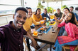 © Xavier Lorenzo - Happy group of multiracial people taking a selfie while having breakfast together on rooftop cafe restaurant - Focus on african man face.