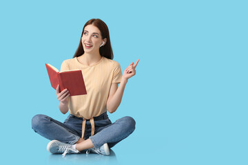 Wall Mural - Young woman with earphones and book on color background