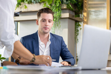 Caucasian business manager is working in eco friendly office surrounding by green plant while his secretary give him approval document to sign