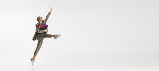 Full-length portrait of happy female employee in classical suit with folder jumping like ballerina isolated over white background. Flyer