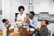 African american family of four eating cookies and drinking juice on bright kitchen. Young parents with two daughters spending morning time for delicious breakfast at home.