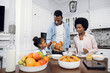 © sofiko14 - Young african parents and their cute daughter having breakfast with fruits and freshly baked buns. Happy family eating together at home. Enjoyment from morning time and no hurry.