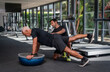© Sergo - An elderly Caucasian man, in the gym, with a personal fitness trainer, in rehabilitation, doing exercises for balance on a gymnastic ball.