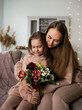 © Яна Айбазова - beautiful mom and daughter in sweatshirts are sitting on the couch and celebrating mother's Day with flowers
