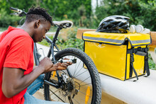 Young Delivery Man Inflating Bicycle By Bench