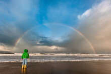 Child In Green Jacket Looking At Rainbow Over An Ocean
