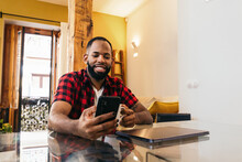 Happy Black Man With Coffee Chatting On Smartphone At Home