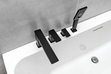 A Modern, Free Standing Wall Mounted Bathtub With A Black Matt Tap, Standing In A Bathroom Lined With Ceramic Tiles.