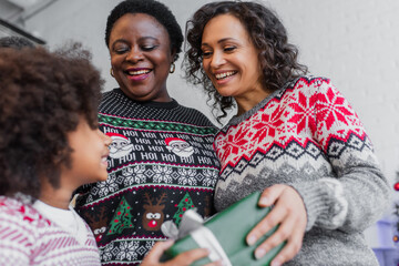 Wall Mural - low angle view of happy african american women giving christmas present to blurred girl