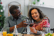 © LIGHTFIELD STUDIOS - laughing african american woman clinking glasses of red wine with dad during christmas dinner