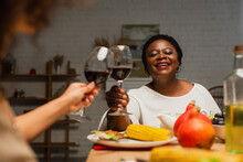 Joyful African American Woman Clinking Glasses Of Red Wine With Blurred Daughter On Thanksgiving Dinner