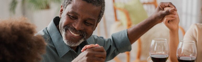 Wall Mural - cheerful african american man holding hands with family during pray on thanksgiving dinner, banner