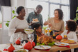 © LIGHTFIELD STUDIOS - African american grandparents holding food near family and thanksgiving dinner