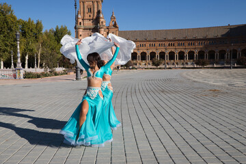 Two young and beautiful belly dancers dancing in a square. They are dressed in light blue with white veils in their hands. World folklore concept from Africa and Asia.