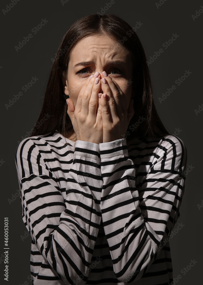 Scared young woman on dark background. Concept of harassment