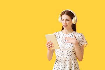 Wall Mural - Displeased young woman with tablet computer listening to audiobook on color background