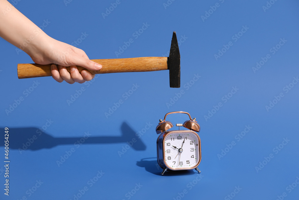 Hammer in hand and alarm clock on blue background