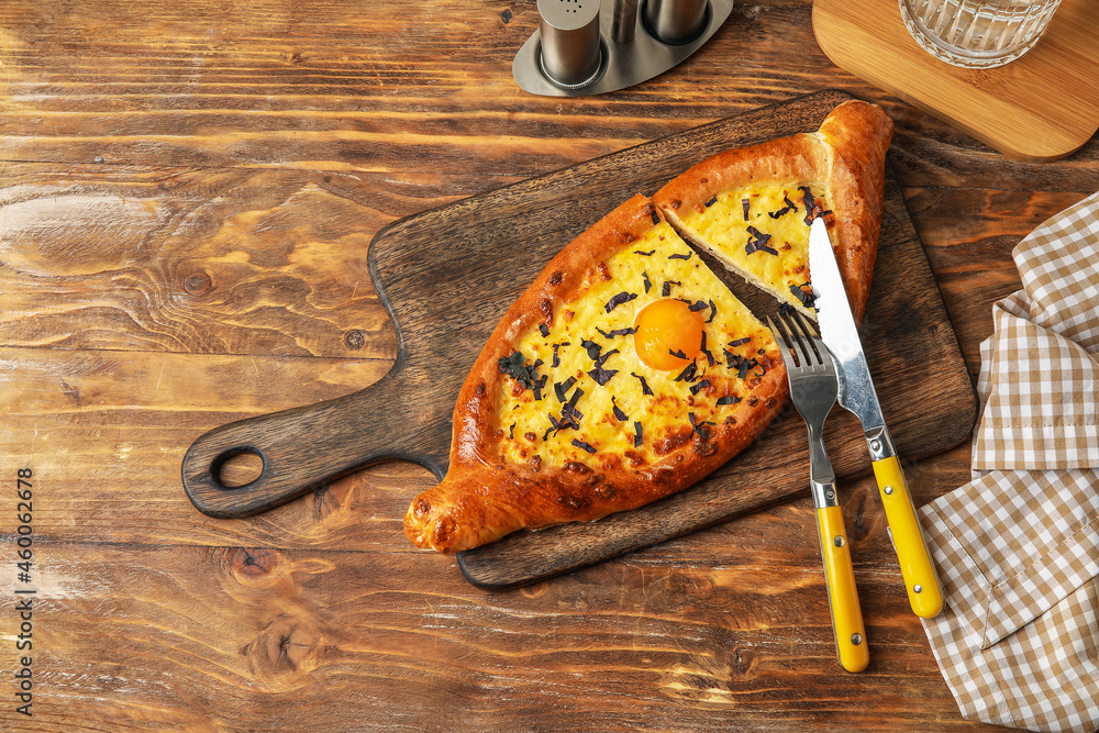 Board with tasty Ajarian khachapuri on wooden background