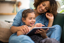 African American Mother And Daughter Watching Entertainment On Digital Tablet At Home