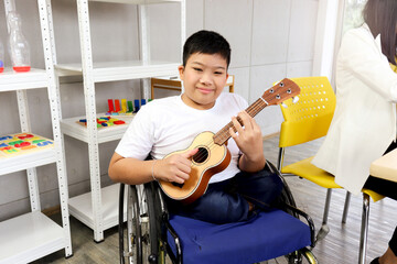 Wall Mural - Happy child having fun during study at school, smiling boy sitting in wheelchair learning to play ukulele, education of kid with physical disability concept.