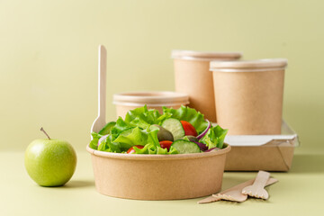 Healthy vegetable salad in recyclable cardboard container. Food delivery, healthy food menu for home or office concept. Green background, side view