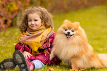 Beautiful Little Girl With Dog In Park In Autumn. Happy Smiling Child Walking With Pomeranian Spitz In Nature In Fall..cute Caucasian Female And Pet Outdoor.