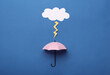 Mini umbrella and paper lighting cloud on blue background, flat lay