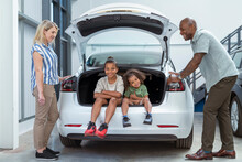 UK, Parents With Daughter And Son Sitting In Car Trunk