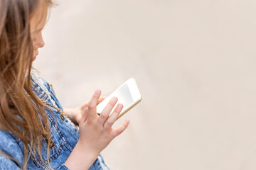 Little girl with a phone in her hands on the street in summer. Copy space for text