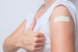 © ReaLiia - A woman showing thimb up and her arm with an adhesive bandage after injection of vaccine. Happy of getting vaccinated from corona virus, covid-19