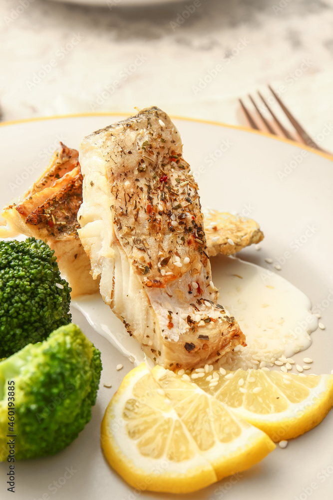Plate with baked cod fillet, sauce and broccoli on grunge background, closeup