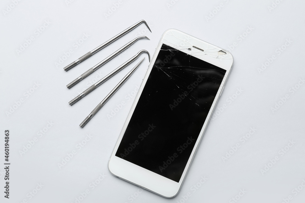 Mobile phone with broken screen and technician tools on light background
