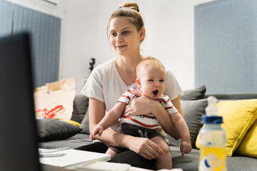 caucasian woman mother holding her small baby child while sitting on the sofa at home