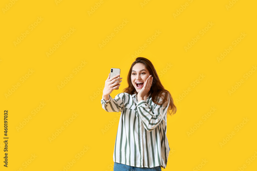 Surprised young woman taking selfie on yellow background