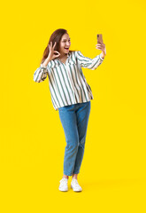 Wall Mural - Beautiful young woman taking selfie on yellow background