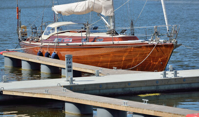 Poster - Elegant modern sailing boat with wooden teak deck moored to a pier in a yacht marina. Nautical vessel, transportation, sport, regatta, recreation, leisure activity, cruise, vacations, lifestyle themes