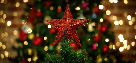 Close up shot of sparkling glossy glitter red star with cute Santa Claus decorating hanging dolls on top of green Christmas pine tree celebrating traditional festive night event on blurred background