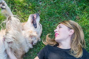 Wall Mural - A young woman lies with a retriever dog on the lawn in the park. Close-up.